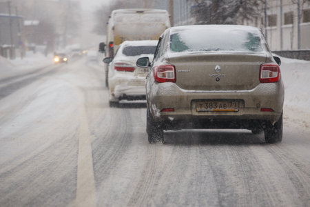 cars driving along snow covered road at winter dayのeditorial素材