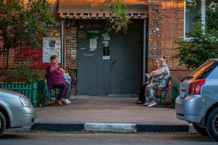 grandmothers sitting on benches in front of apartment building entrance and chattingのeditorial素材