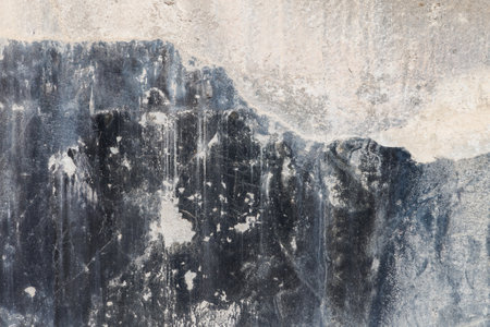 old concrete wall with black paint leftovers covered with whitewash stains, full-frame background and textureの写真素材
