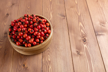 red dog-rose rosehip fruits in a wooden bowl on wooden tableの写真素材