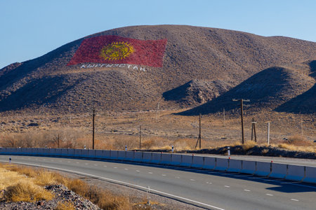 The flag of Kyrgyzstan is drawn on a mountain at sunny autumn day, showcasing the nations pride and spirit.の写真素材