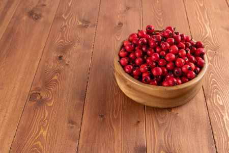 red hawthorn berries in wooden bowl on flat wooden surfaceの写真素材