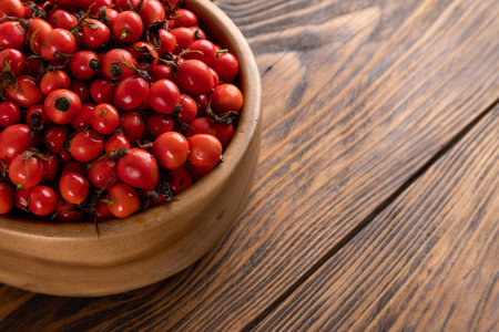 red dog-rose rosehip fruits in a wooden bowl on wooden tableの写真素材