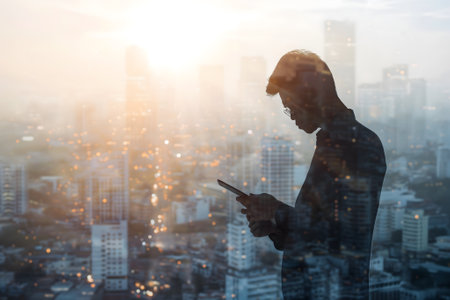 Double exposure of business and a city - Asian businessman using a digital tablet superimposed on a city skylineの素材