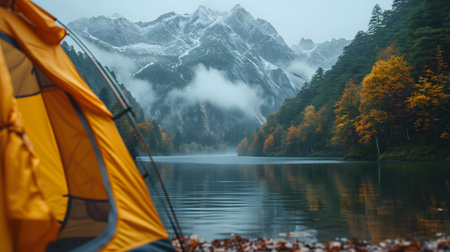 Close-up of a tent in the foreground and mountains with fog in the background with a lake or river in the foreground.の素材