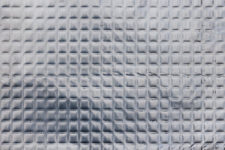 Closeup full-frame background and texture of aluminum coated butil rubber sheet with square pattern.