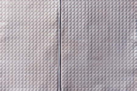 Closeup full-frame background and texture of aluminum coated butil rubber sheet with square pattern.