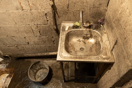 Dirty toilet room stainless steel sink with a bucket on the floor, uncoated concrete flooring and cinder brick walls.の写真素材
