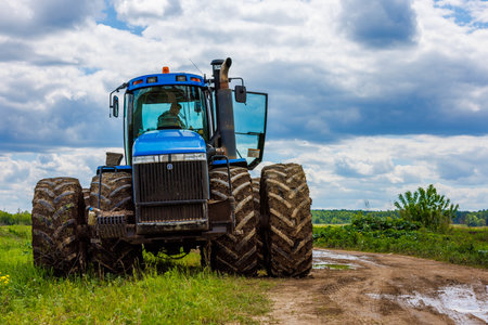 Blue tractor with double wheels standing near agricultural field at hot sunny day.のeditorial素材