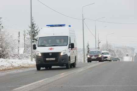 white ambulance minibus with two women inside the cabin driving along winter road at cloudy dayのeditorial素材