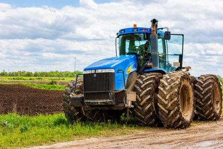 Blue tractor with double wheels standing near agricultural field at hot sunny day.のeditorial素材