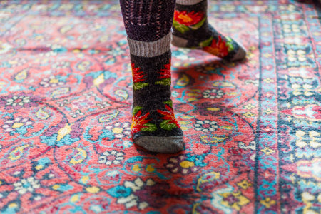legs in warm woven wool socks standing on red ornate carpet floor at homeの写真素材