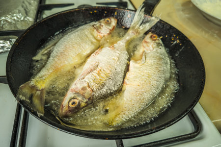 three whole freshwater fish frying with flour in old cast iron skilletの写真素材