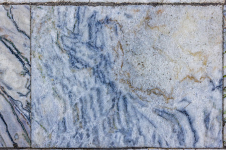 Close-up of aged and textured marble floor tiles featuring prominent blue and gold-toned veins on a white and grey base, showing signs of wear and timeの写真素材