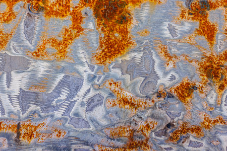Close-up of a unique metal texture featuring partially grinded white and bluish-gray paint revealing areas of orange-yellow rust. Visible grinding marks coexist with rounded rust spots, creating an abstract pattern.の写真素材