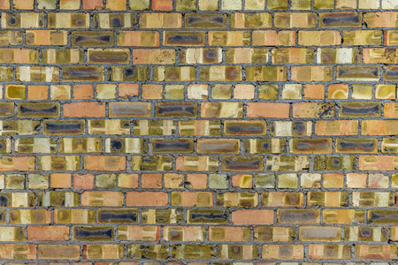 A close-up of a weathered brick wall, showcasing a mix of yellow, green, and brown hues with natural...