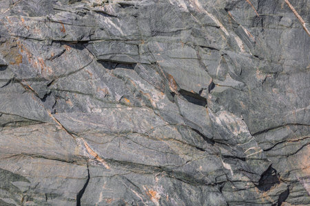 Detailed view of a rugged metamorphic rock surface with numerous cracks and fissures, exhibiting...