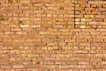 A full-frame shot displays an old brick wall with a visibly weathered texture, exhibiting signs of...