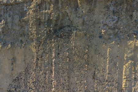 Rough, uneven concrete surface embedded with small pebbles and showing signs of age and wear under...
