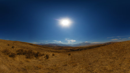 A wide panoramic view of arid, yellow-brown rolling hills under a clear blue sky with the sun...