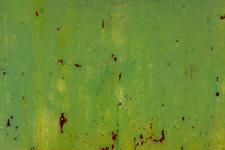 Close-up of a weathered metal surface exhibiting rust, scratches, and peeling green paint. Outdoor industrial setting during daytime conveys a distressed, aged mood.の写真素材