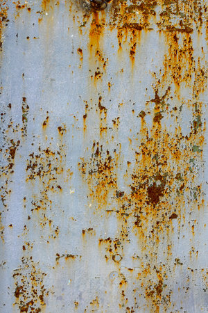 Rusted metal surface displays significant peeling paint and weathered texture in an outdoor urban...