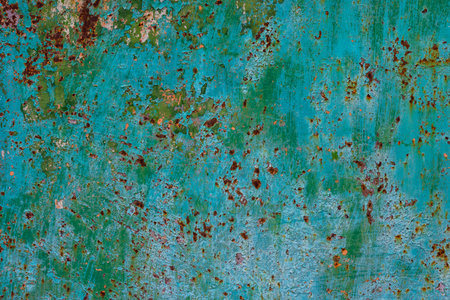 Weathered green metal surface displays rust and peeling paint in an industrial outdoor setting....