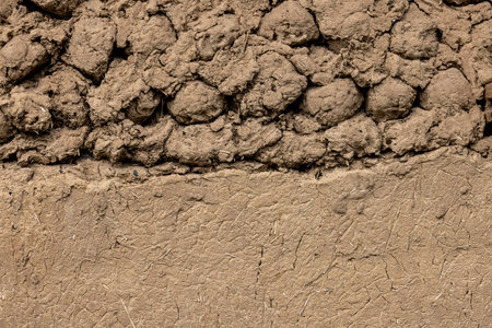 Rustic adobe wall texture partially plastered with same material.