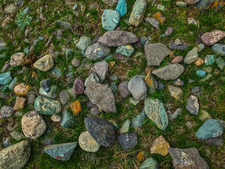 Numerous rocks of varying sizes, shapes, and colors scattered across grassy ground. Serene outdoor...