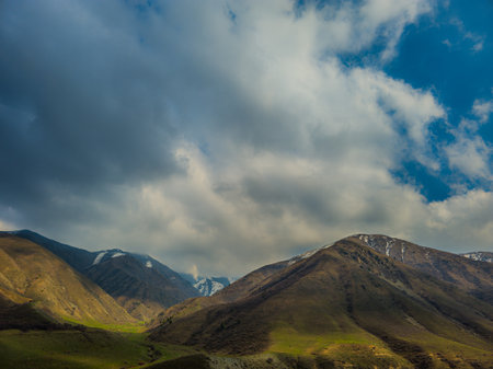 Dramatic view of mountains in serene valley with stormy clouds above at spring day in Kyrgyzstan.