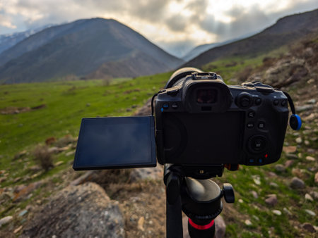 Black photo camera on tripod placed on grassy field captures stunning mountainous landscape.の写真素材