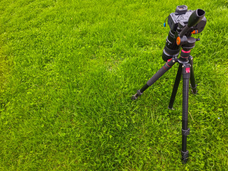 Camera sits on tripod in peaceful grassy field under clear blue sky. Natural light enhances tranquil outdoor setting, inviting exploration and creativity.の写真素材