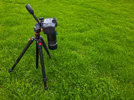 Camera placed on tripod in a peaceful grassy field under clear blue sky. Scene evokes tranquility and inspiration, perfect for outdoor photography enthusiasts.の写真素材
