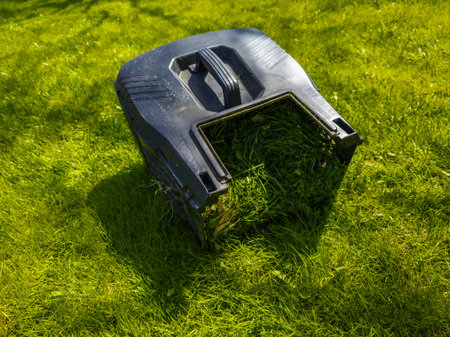 Grass catcher sits filled with freshly cut grass in a peaceful garden. Sunlight filters through trees, creating a serene outdoor atmosphere during daytime.の写真素材
