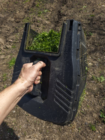 Adult man with light skin holds a container filled with freshly cut grass while standing in a garden...