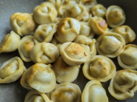 Close-up of many dumplings sizzling in a frying pan, capturing the warmth and comfort of home cooking.の写真素材