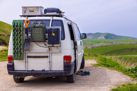 White van parked peacefully on roadside in rural area. Surrounding grassy hills create a serene atmosphere, showcasing adventure gear like storage containers and jerry cans.の写真素材