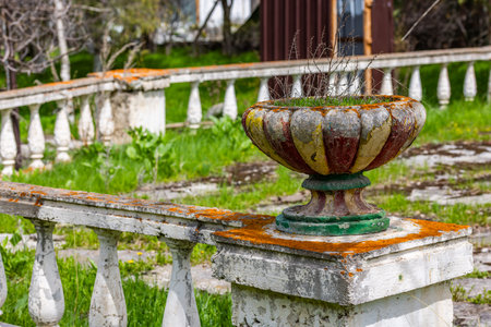 Decaying soviet era ornate planter contains dried plants and moss, showing its age with faded multicolored paint. Stone balustrade sections create a serene, weathered atmosphere in a neglected garden.の写真素材