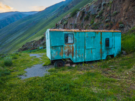 Rusty teal trailer abandoned on grassy area near mountainsの写真素材