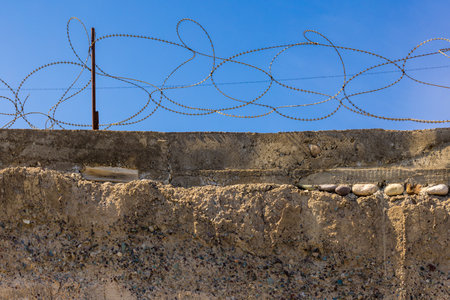 Concrete wall with barbed wire against a clear blue sky. Security barrier.の写真素材