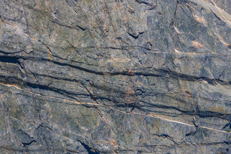 Foliated metamorphic rock with prominent fractures, natural texture, outdoor, daylight