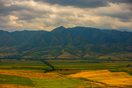 Serene rural landscape with mountains, hills and village under overcast skyの写真素材