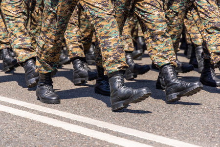 Soldiers in camouflage clothing marching in formation on asphalt roadの写真素材
