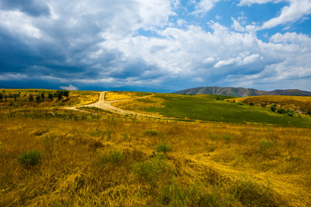 Rolling hills and dirt road under cloudy sky in autumnal Kyrgyzstanの写真素材