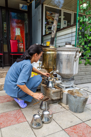 Cholok, Kyrgyzstan - July 16, 2024 - Adult woman pouring tea from samovar outdoors in daylightのeditorial素材