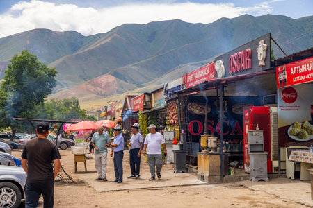 Cholok, Kyrgyzstan - July 16, 2024 - Four men walking in bustling outdoor roadside cafe near mountainsのeditorial素材