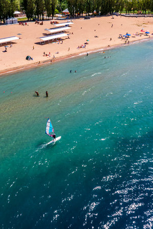 Dolinka, Kyrgyzstan - July 17, 2024 Windsurfer enjoying summer day at sandy beach with beachgoersのeditorial素材