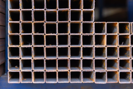 Close-up view of stacked square metal tubes showcasing rust and wear. Textured surfaces create a striking contrast between warm patina and dark shadows.