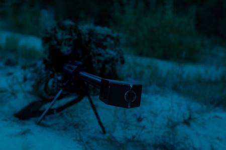 Army sniper with big rifle lying in wait in the forest at nighttimeの写真素材