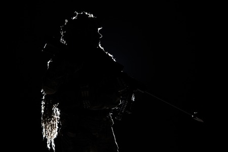 Army sniper with big rifle standing on black background. Backlit contour silhouette shot. Invisible death conceptの写真素材